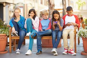 Children sitting on a park bench looking at their smart devices